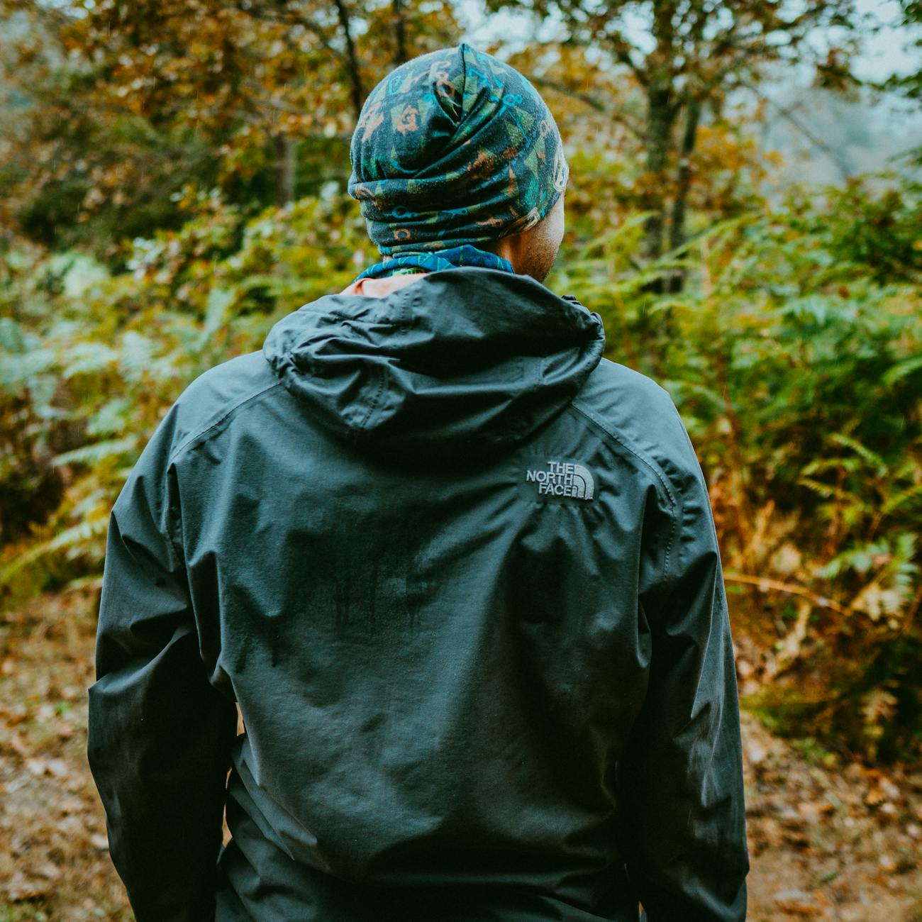 Randonneur sous la pluie en forêt cherchant un abri équipé d'une cape de pluie et d'un sac à dos