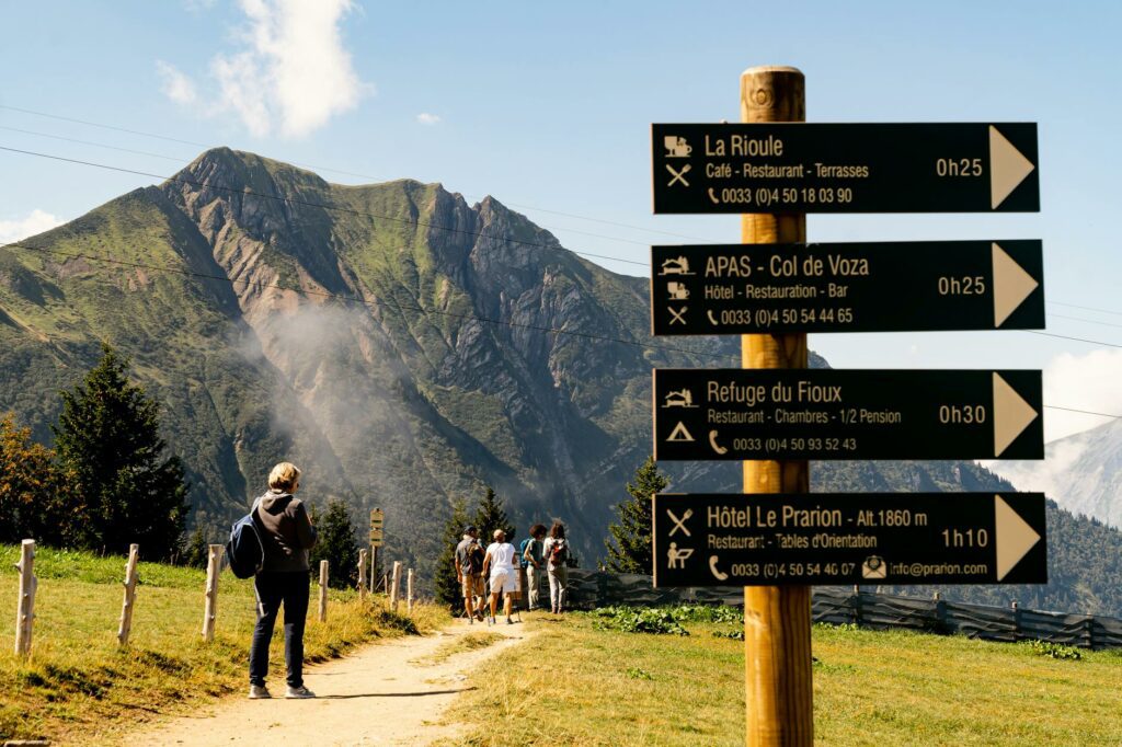 Une famille en randonnée sur un sentier de montagne ensoleillé en France, avec enfants et sac à dos, paysage verdoyant en arrière-plan