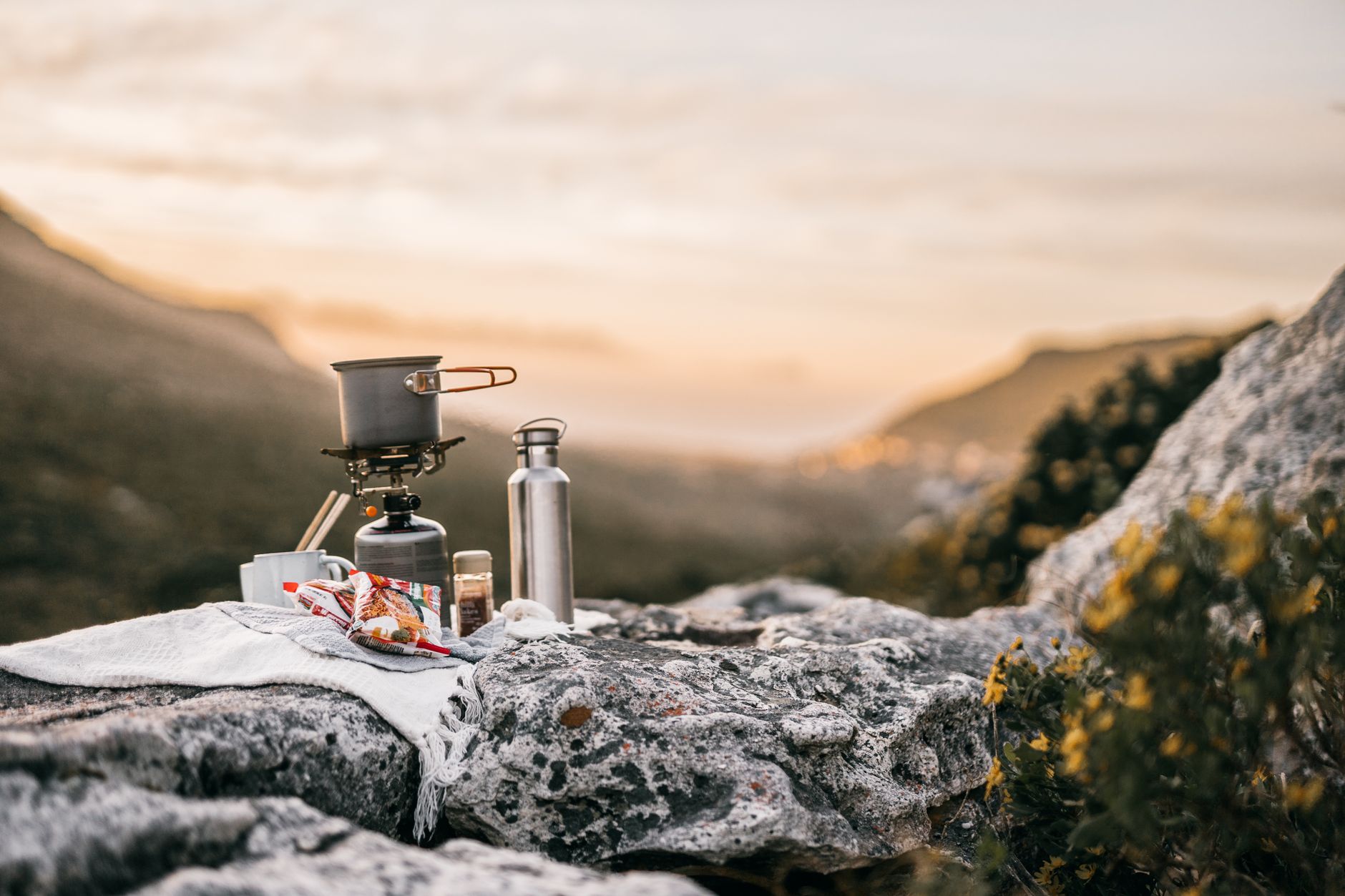Randonneur préparant un repas chaud au réchaud devant un bivouac en montagne au lever du jour