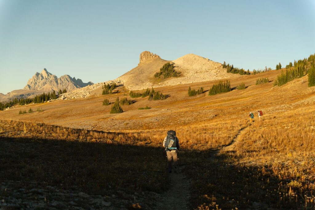 Randonneur épuisé assis sur un sentier de montagne au coucher du soleil, jambes lourdes après un effort prolongé en randonnée