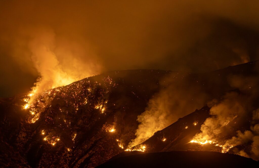 Fumée d'incendie de forêt s'élevant au-dessus d'un massif montagneux boisé, illustrant les fermetures de sentiers de randonnée en France durant l'été 2026