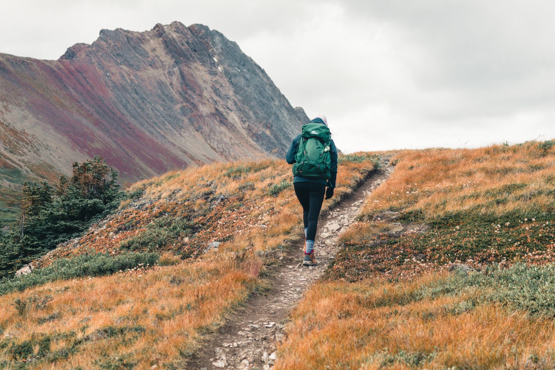 Randonneur équipé d'un sac à dos progressant sur un sentier de montagne, matériel outdoor choisi avec soin