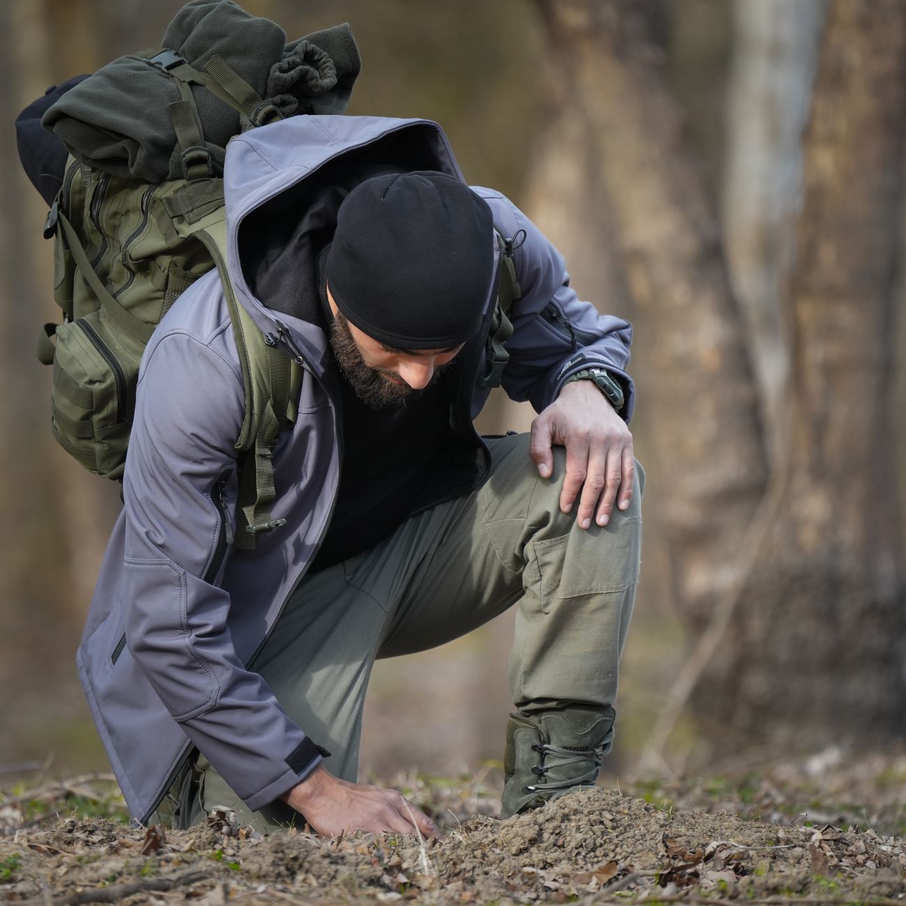 Randonneur équipé d'un sac à dos de trek et de chaussures montantes, accroupi sur un sentier forestier