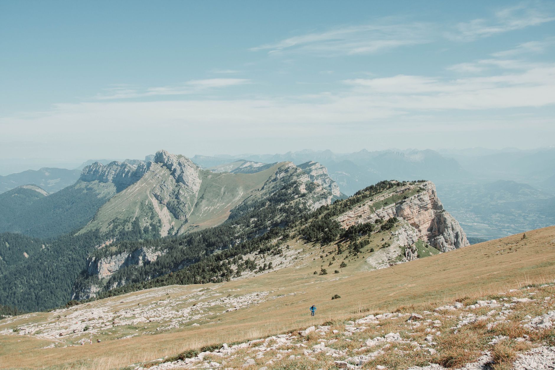 Randonneur observant un panorama de sommets alpins enneigés depuis un sentier de crête en fin de journée.