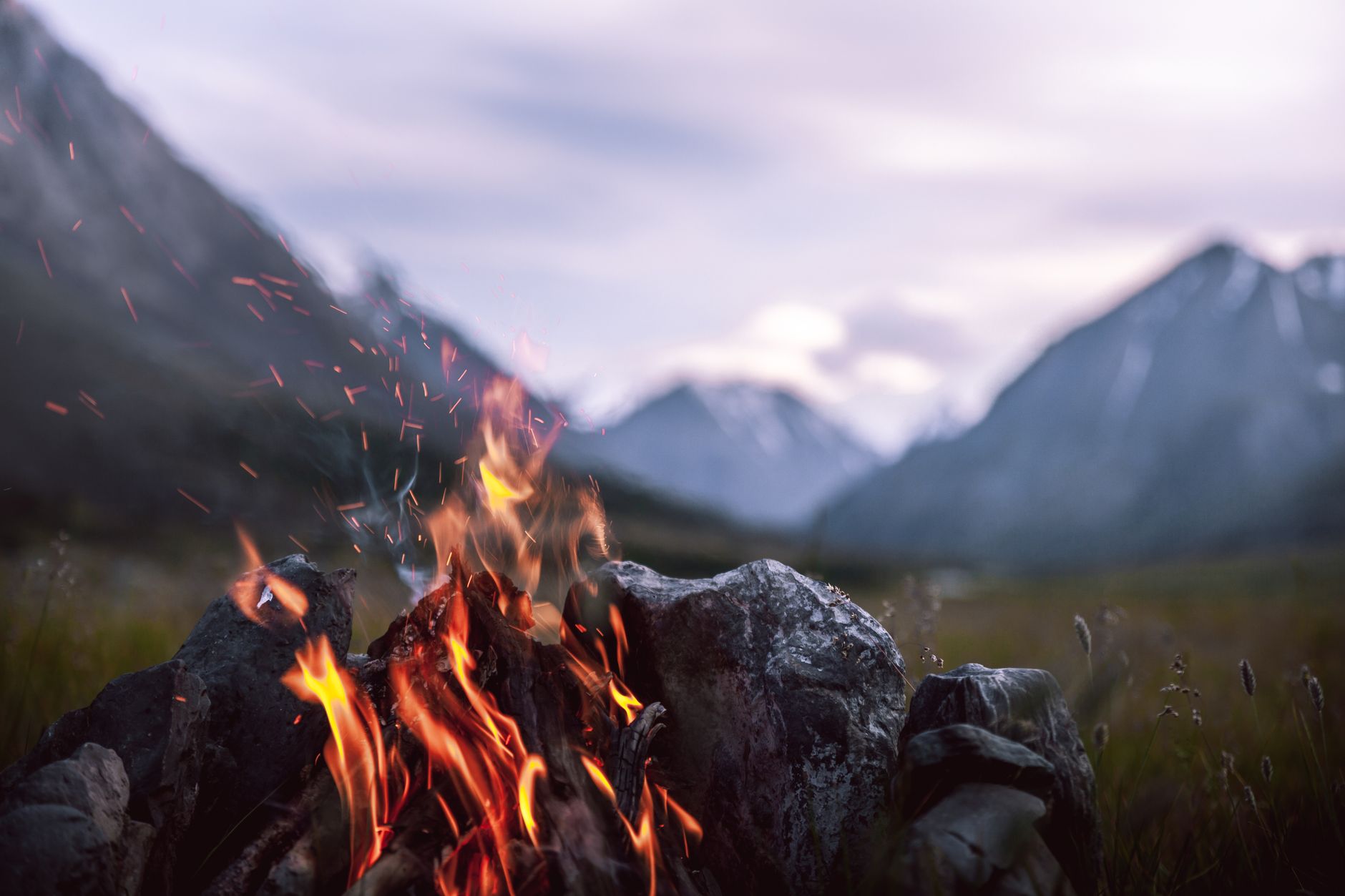 Feu de camp crépitant au crépuscule dans un paysage de montagne sauvage, flammes orangées devant les sommets