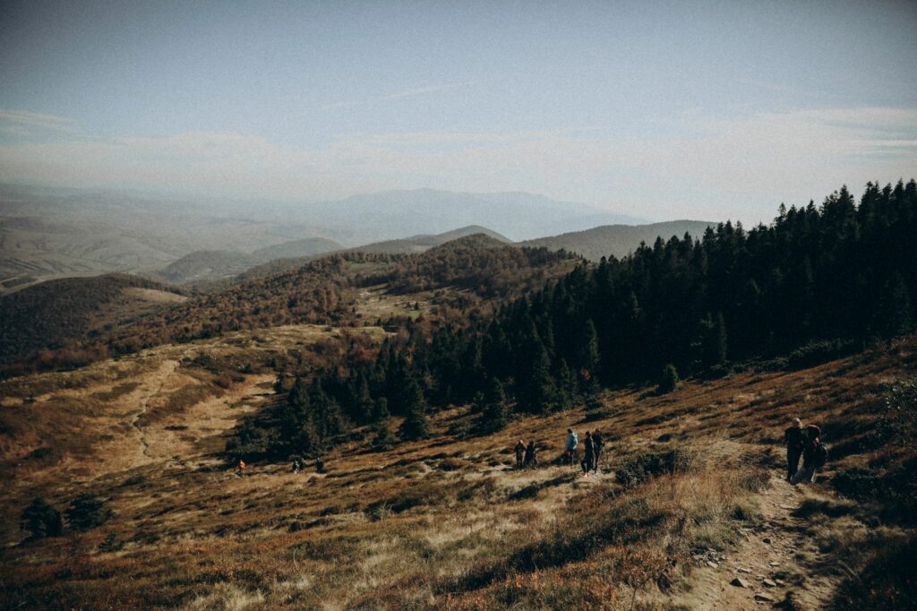 Randonneurs sur une crête de moyenne montagne en automne, forêts de feuillus roussies et résineux sombres