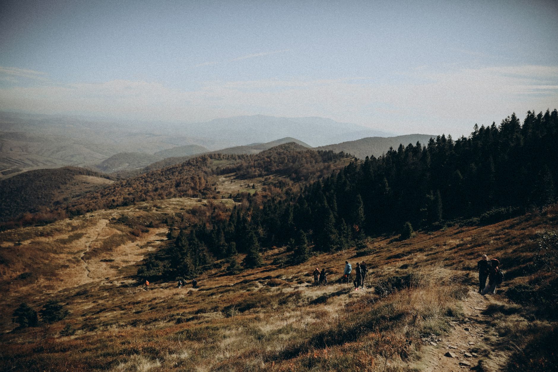 Randonneurs sur une crête de moyenne montagne en automne, forêts de feuillus roussies et résineux sombres